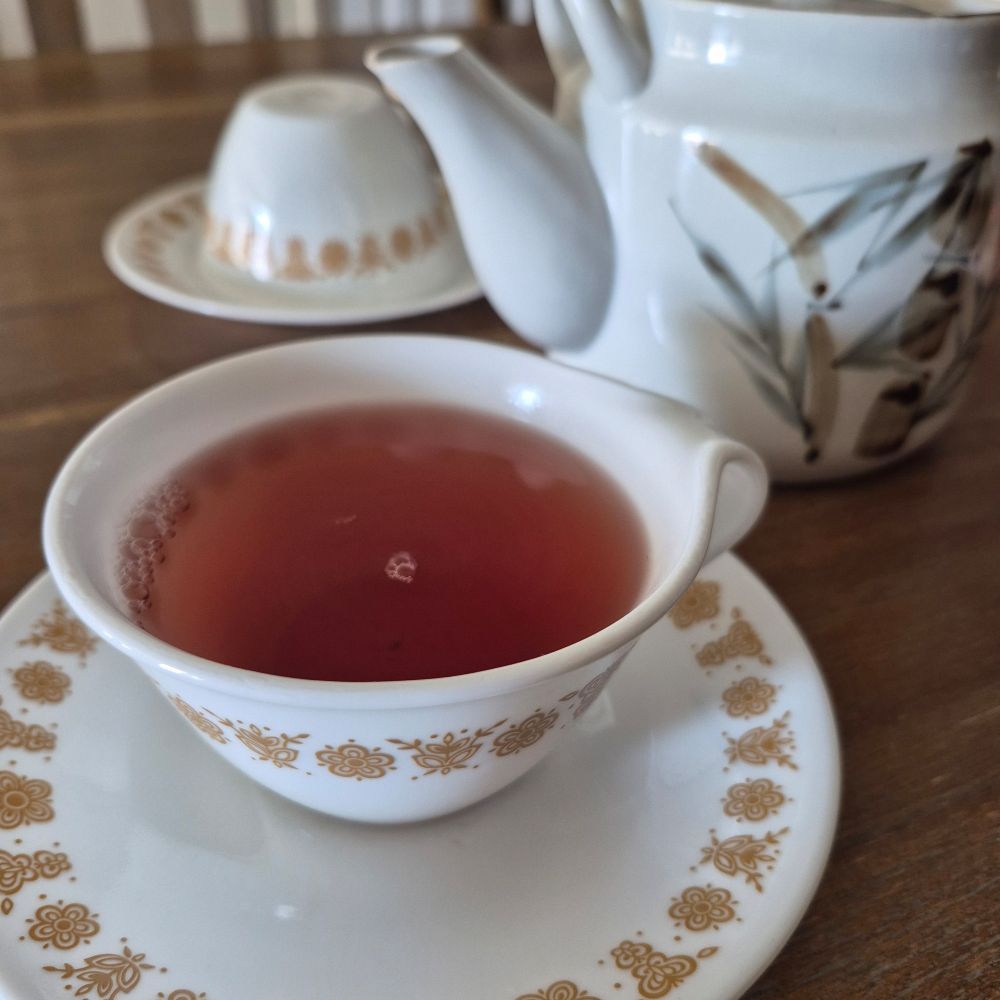 A cup of HEB superberry green tea in front of a teapot and another cup and saucer