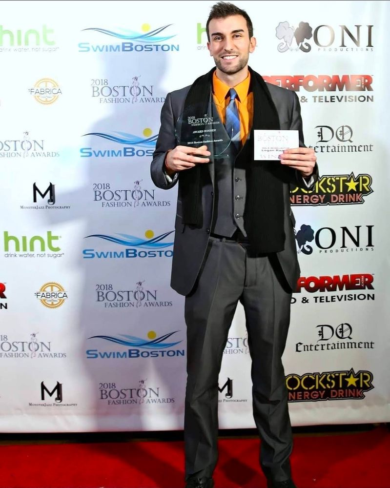 An actor receiving the boston actor of year award in 2018. They are wearing a 3 piece gray suit, an orange dress shirt and a blue tie. 
