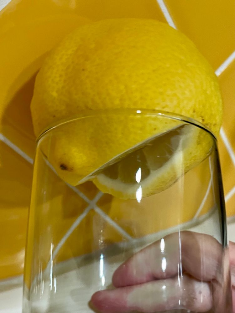 A lemon, with a slice removed, placed on top of a clear drinking glass—cut side down facing the bottom of the glass