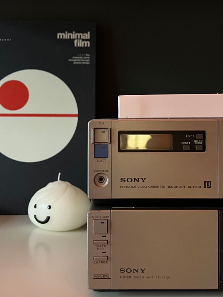A Sony Betamax cassette recorder and tuner on the right. To its left is a small round candle with a smiling face and a book: “Minimal Film”