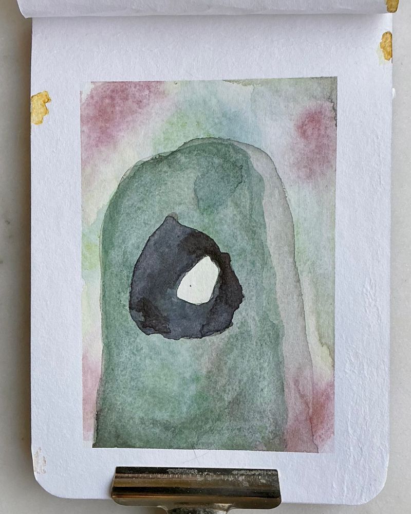 A green rounded rock with a hole in the center that lets you see through to the other side in watercolor on A6 paper