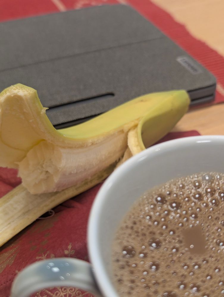 Kaffekopp, banan och surfplatta på ett bord