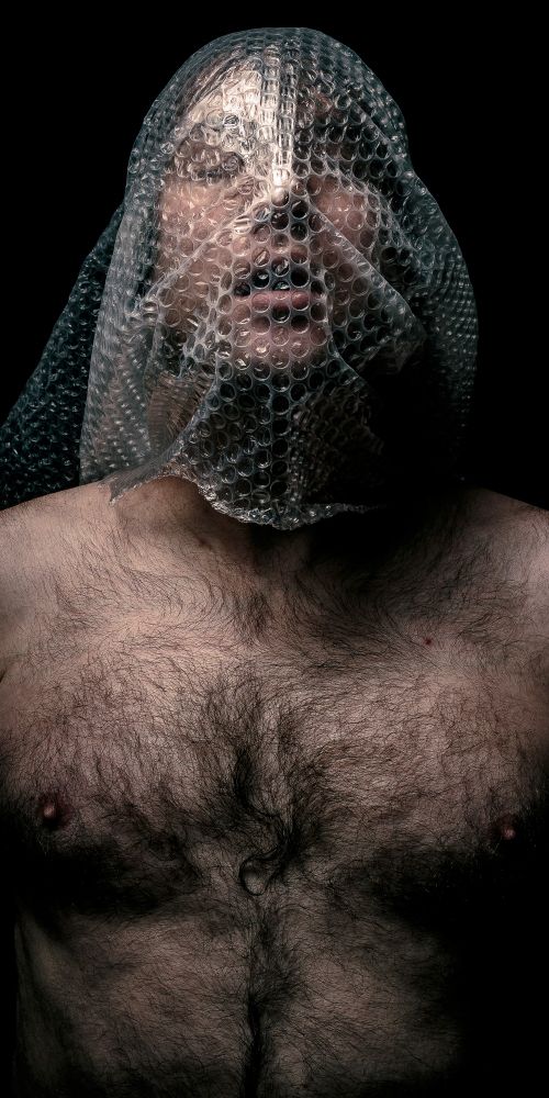 I stand framed from the waist up with no shirt and my head in bubble wrap. 