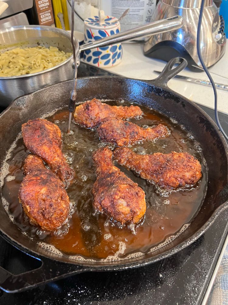 Chicken drumsticks being fried in a cast iron pan. 