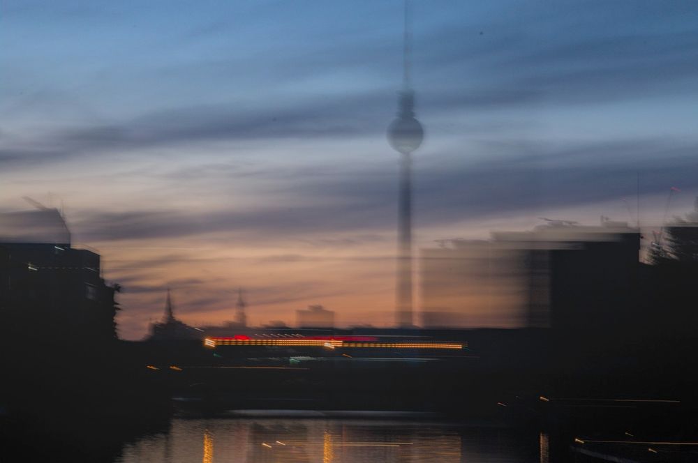 Aufnahme vom #Fernsehturm am #Alexanderplatz und der #Spree #Berlin zur #BlaueStunde. Unscharfe, verwischte Silhouetten und Lichter in schwarz-orange-blau Tönen.