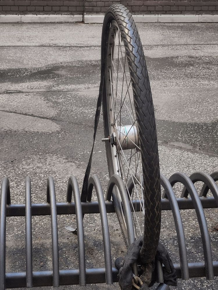 Vorderrad ohne Fahrrad, im Fahrradständer festgeschlossen und mit leicht glänzendem Reifen.