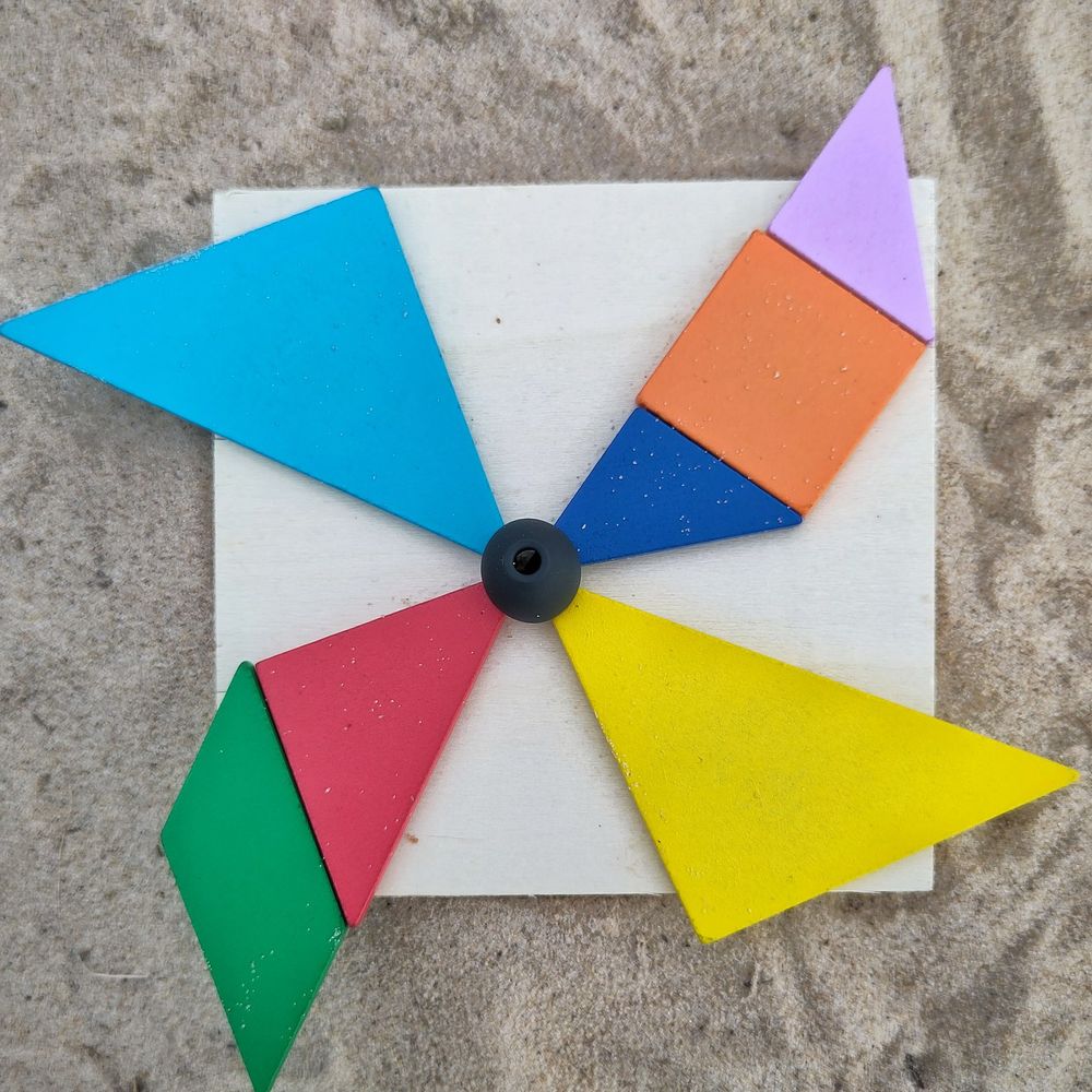 Bunte #Tangram-Plättchen in Form eines Windrades, auf hellem Holzquadrat im #Kniepsand