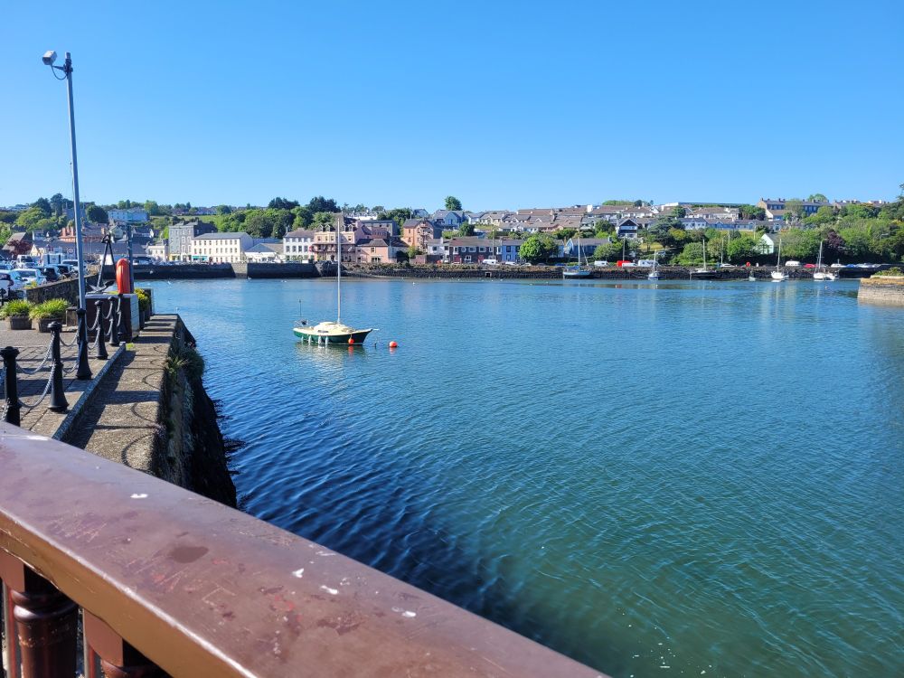 Railing overlooking water with a boat in the background, behind that is Kinsale, Ireland with its buildings on the water 