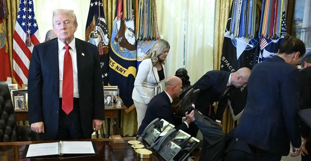 A group of people attending to another lying on the floor. President Trump stands behind the Resolute desk, shoulders slumped, facing the camera with a look of absolute boredom on his face. 