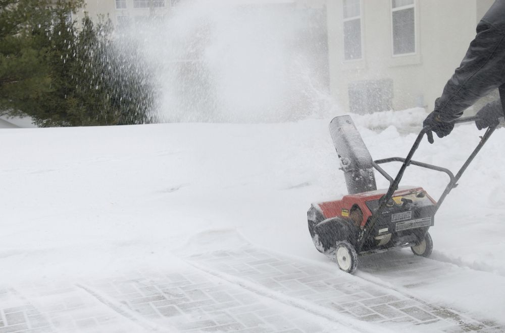 A snowy driveway being cleared by a snowblower