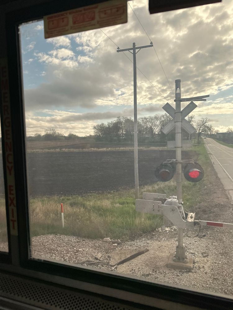 View from a train window in Wisconsin, showing some farmland, a railroad crossing, and a rural road. 