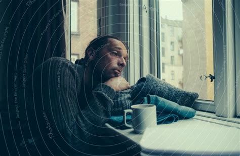 Mann der scheinbar gelangweilt mit Kissen am Fenster hängt 