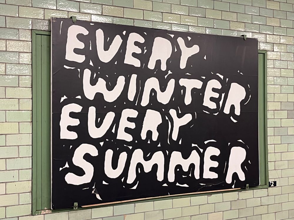 Großes Plakat, weiß auf schwarz: „EVERY WINTER EVERY SUMMER“ auf hellgrünen Kacheln
