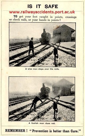 Posed railway staff safety photo, black and white, showing a worker having caught his foot between rails whilst crossing tracks, and an oncoming train about to run him over.