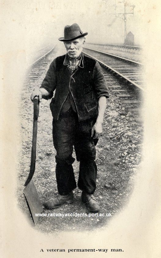 1920s photograph, showing an old track worker, holding a shovel, stood between two railway lines, with hut and signals in the background. Caption reads ‘A veteran permanent-way man’.