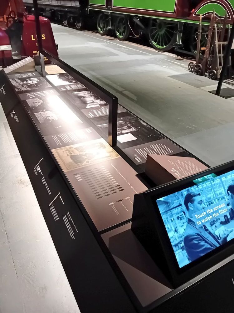 Interpretation board, with project infographic, and steam engine and stock behind.