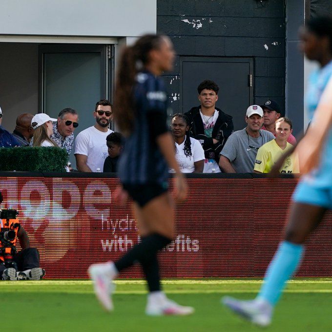 Ben Shelton in a field suite with a blurry Trinity Rodman in action in the foreground