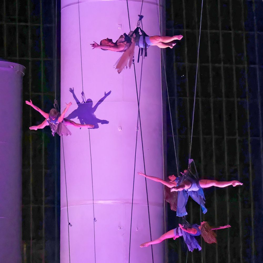 Four ladies performing while suspended with cables from large smokestacks at an unused power plant.