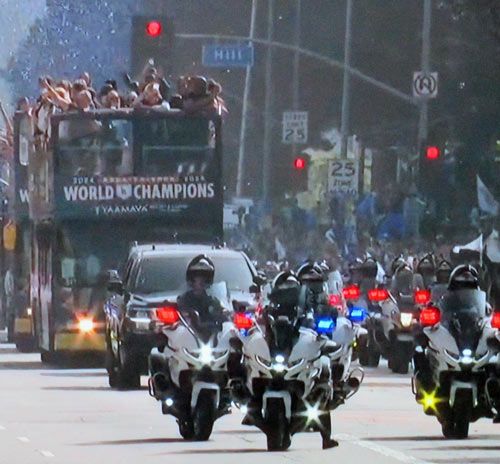 Dodgers, friends, and families on double double-decker bus being escorted by cops on motorcycles through Downtown Los Angeles