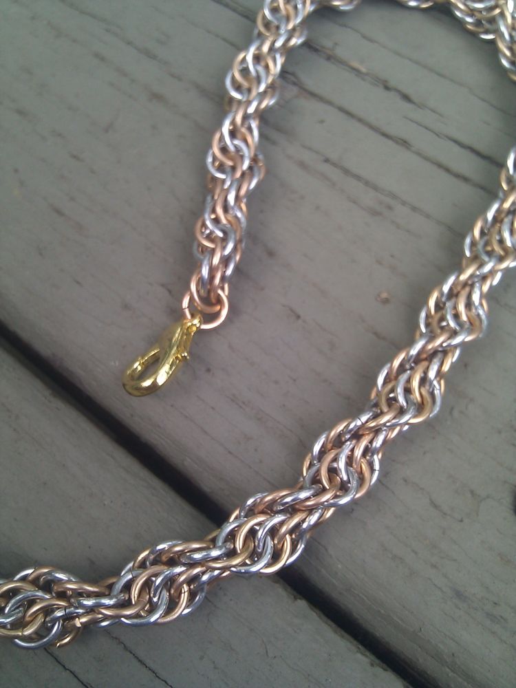 A picture of a necklace made of two individual spirals made of brass and bright aluminium rings, wound together into a greater spiral.