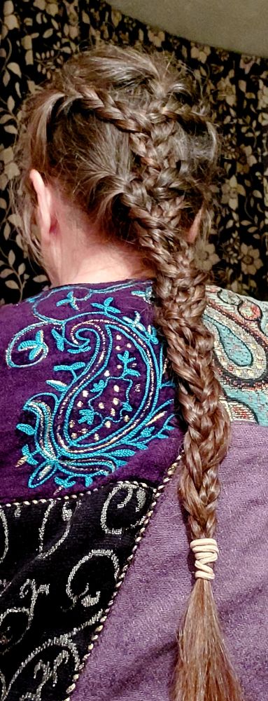 View of the back of a woman's head of mid- brown hair worn in a long braid plaited from several narrower braids.