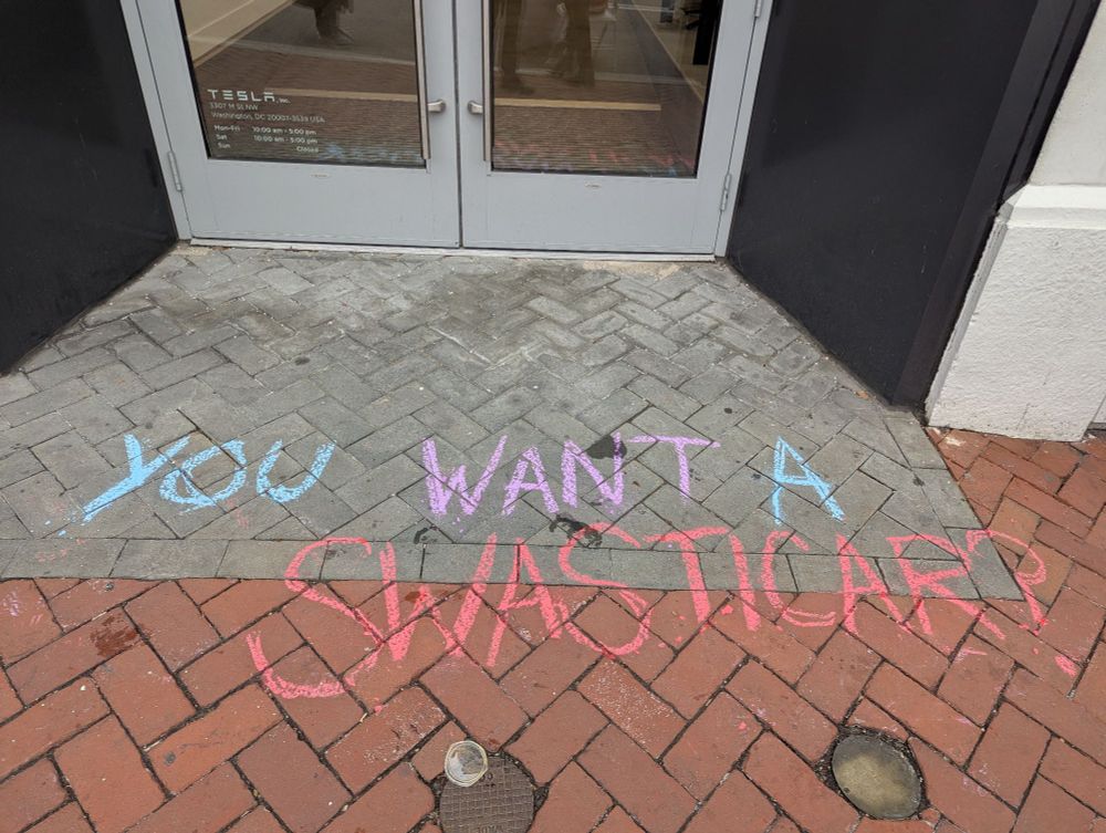 Chalk art in front of Georgetown DC Tesla: "YOU WANT A SWASTICAR?" 