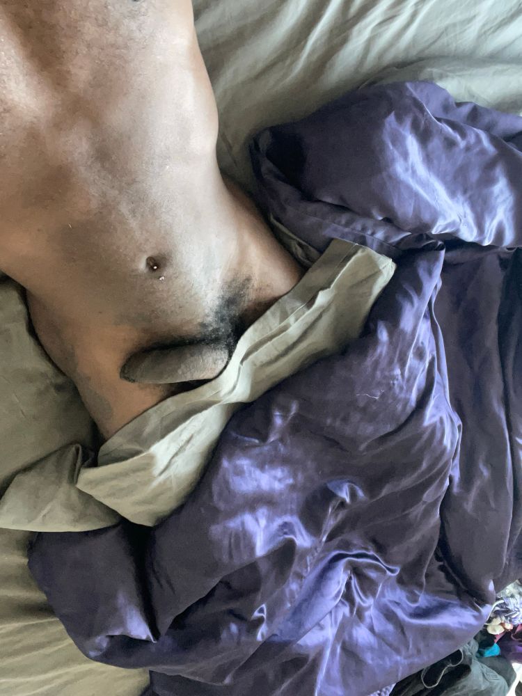 Me laying on a messy bed, blanket and covers pulled up just below my dick. My soft dick is facing up and leans over to the right, foreskin covering the head.