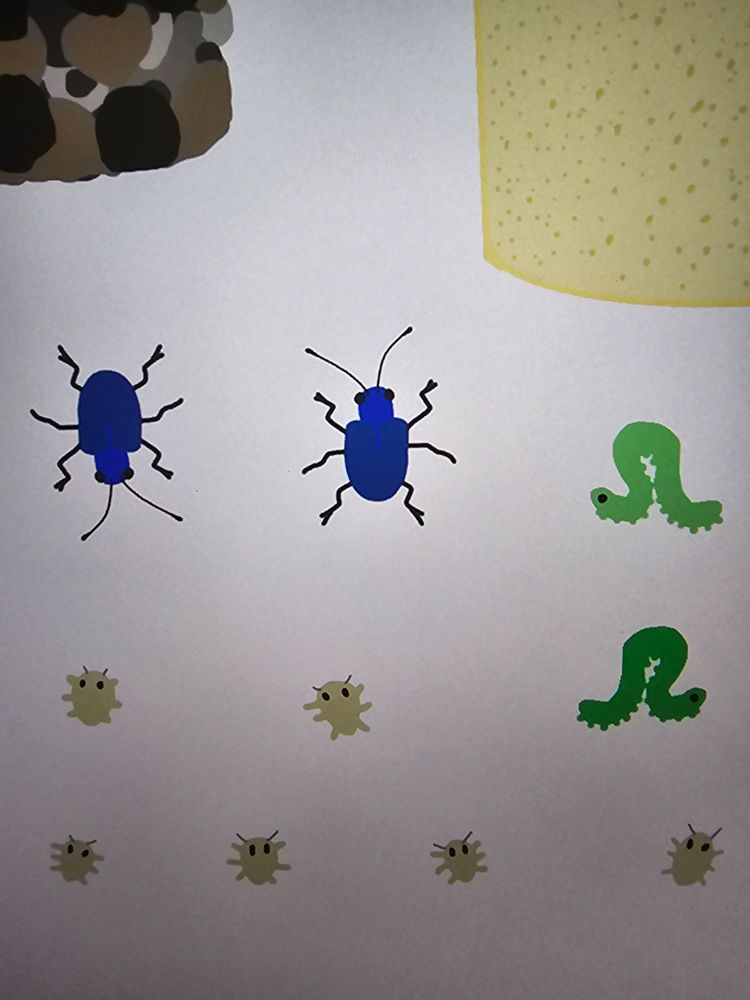 A close up picture of an IPad screen, showing two drawn blue beetles, inch worms, mites, sand and rocks. 