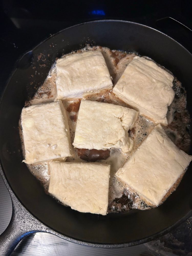 a cast iron skillet with brown butter and six square-ish buttermilk biscuits about to be baked