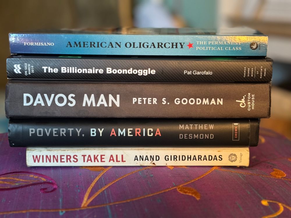 Stack of books, bottom top, *Winner take all* by Anand Giridharadas, *Poverty, by America” by Matthew Desmond, *Davos Man* by Peter S. Goodman, *The Billionaire Boondoggle* by Pat Garofalo and *American Oligarchy* by Ron Formisano
