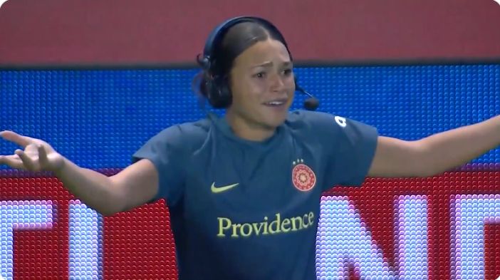 Photo of Sophia Smith, headset on, arms and palms up in questioning motion, eyebrows scrunched with a “WTF” facial expression, as she realizes her teammates are taking a photo without her