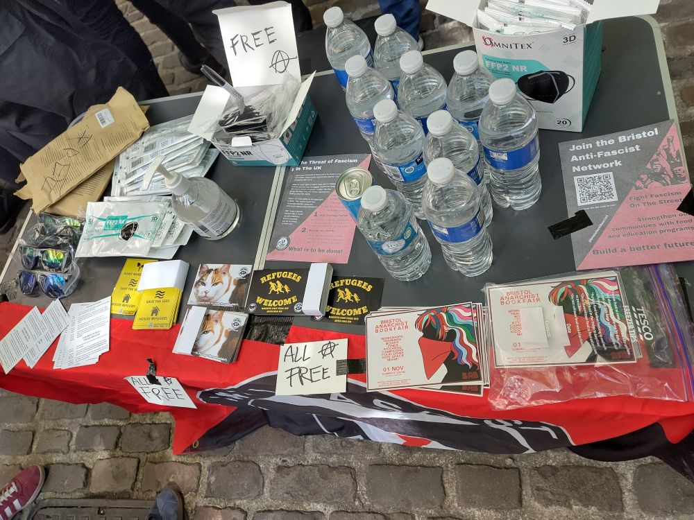 A stalk on a street with stickers, masks, and bottles of water 
