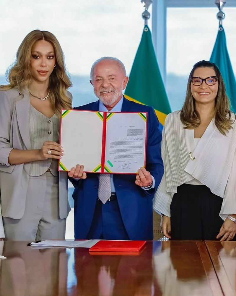 Foto minha segurando, com Lula, o documento da sanção da Lei. Ao nosso lado está a Primeira-Dama Janja Lula da Silva.