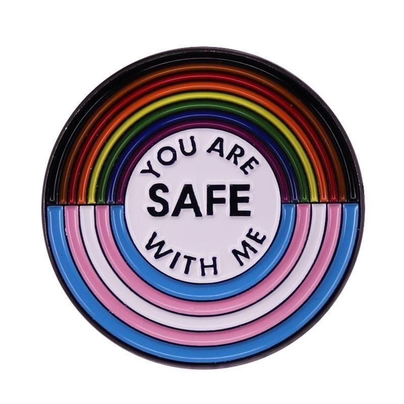 A circular badge with the upper semi-circle in Progress Pride rainbow colours and the lower semi-circle in Trans Flag colours, with the centre reading 