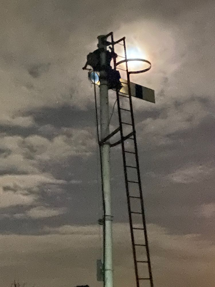 Railway semaphore signal backlit by the moon in a cloudy sky