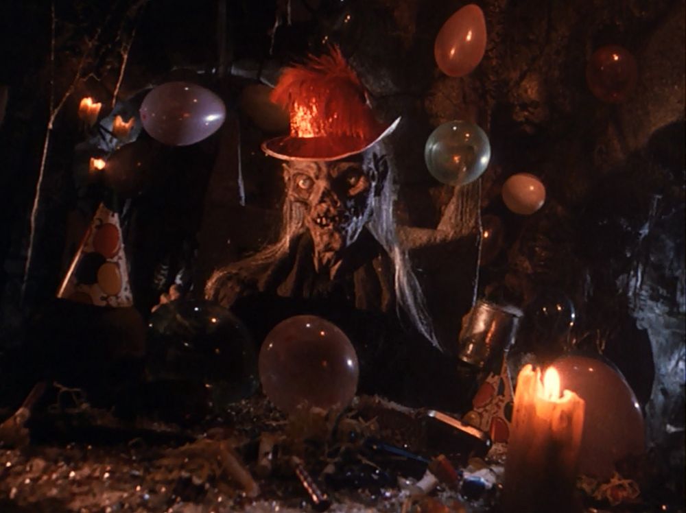 Mummy corpse with a party hat on sitting in a dark crypt with party decorations