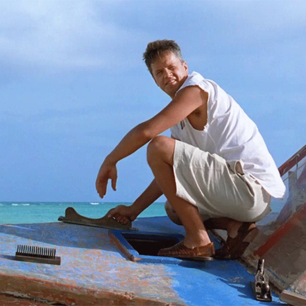 a man squatting on a blue boat with a comb on the ground