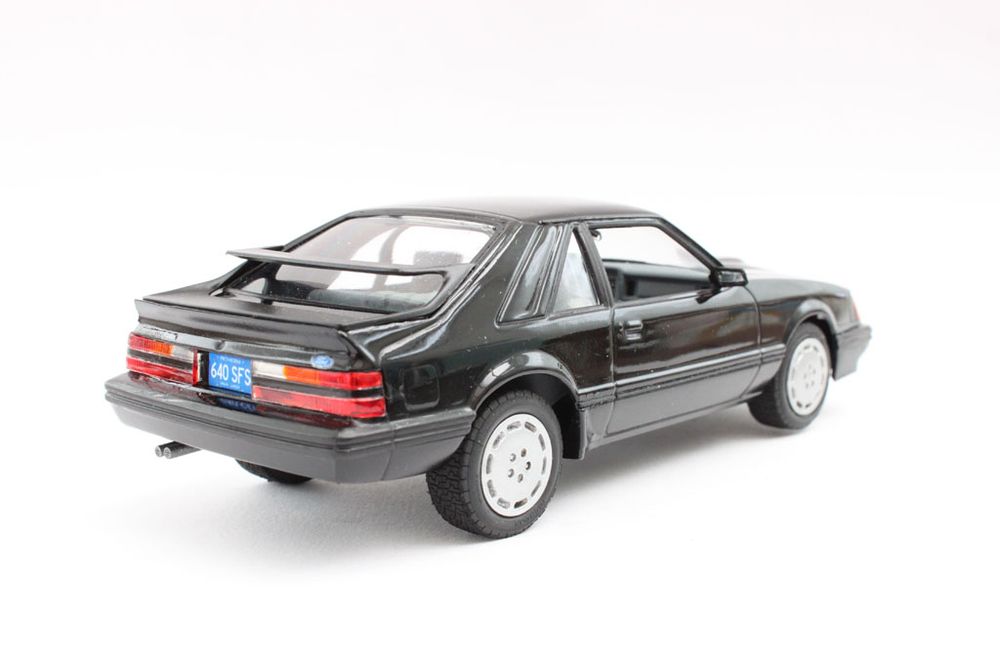 1/24 scale plastic model of a 1985 Ford Mustang SVO, built from the Monogram kit, painted black, with a grey interior.  Rear right three-quarter view.