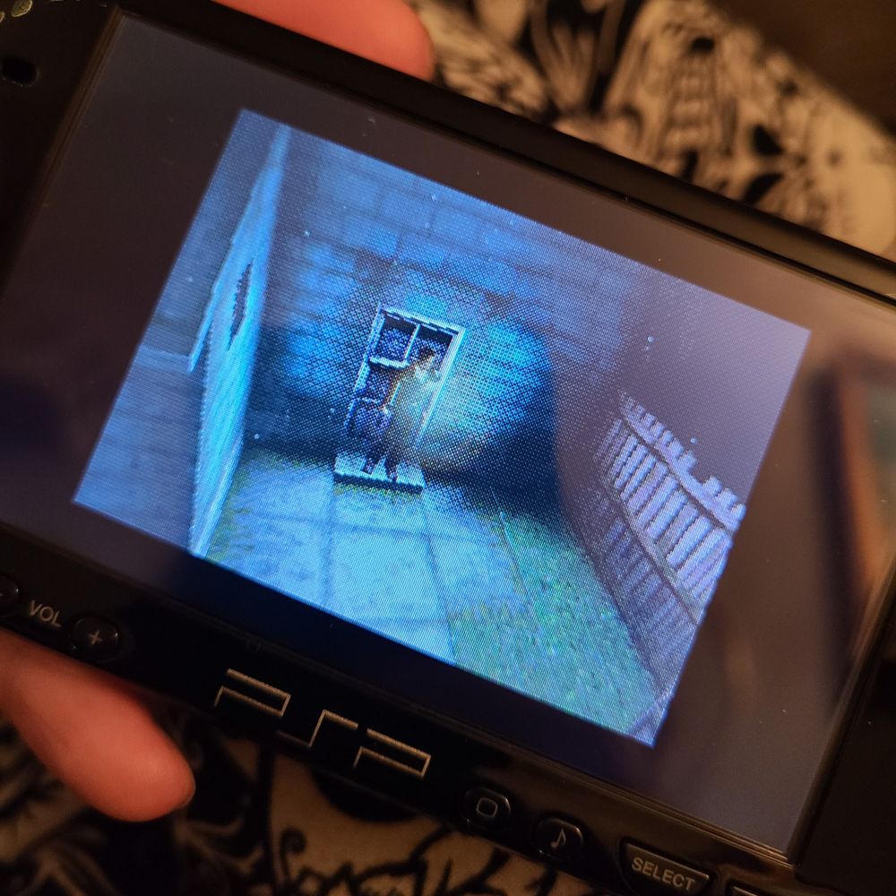 holding a psp; displayed on the screen is harry mason standing in a back yard with his flashlight on