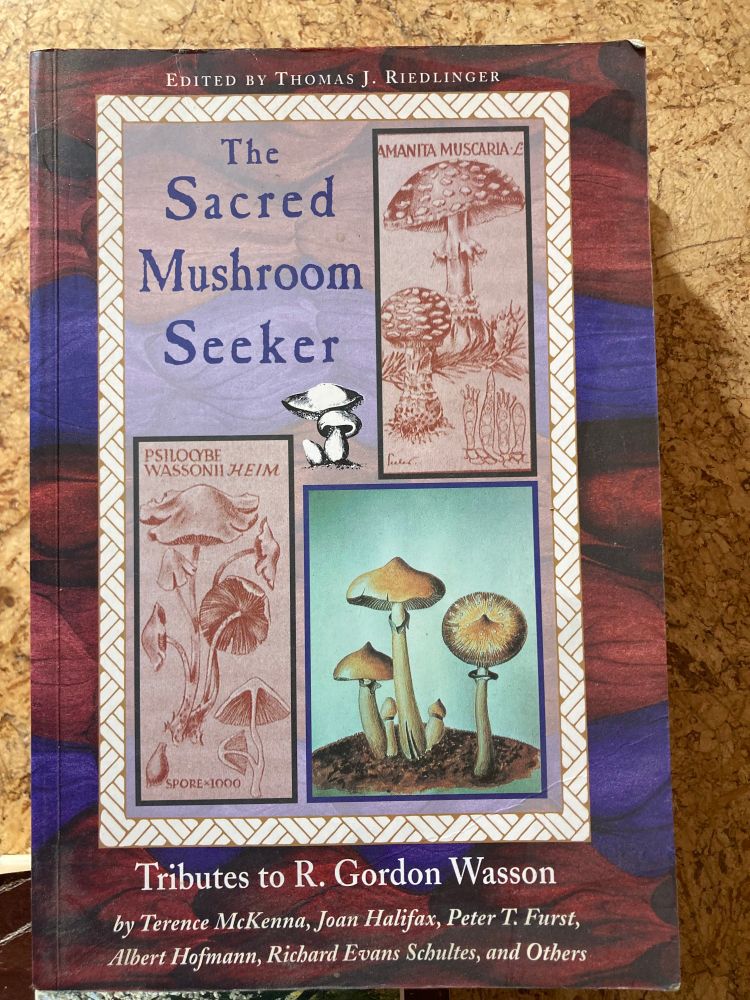 Book cover of The Sacred Mushroom Seeker: Tributes to R. Gordon Wasson edited by Thomas J. Riedlinger, featuring vintage-style botanical illustrations of mushrooms, including Amanita muscaria, on a richly colored background.