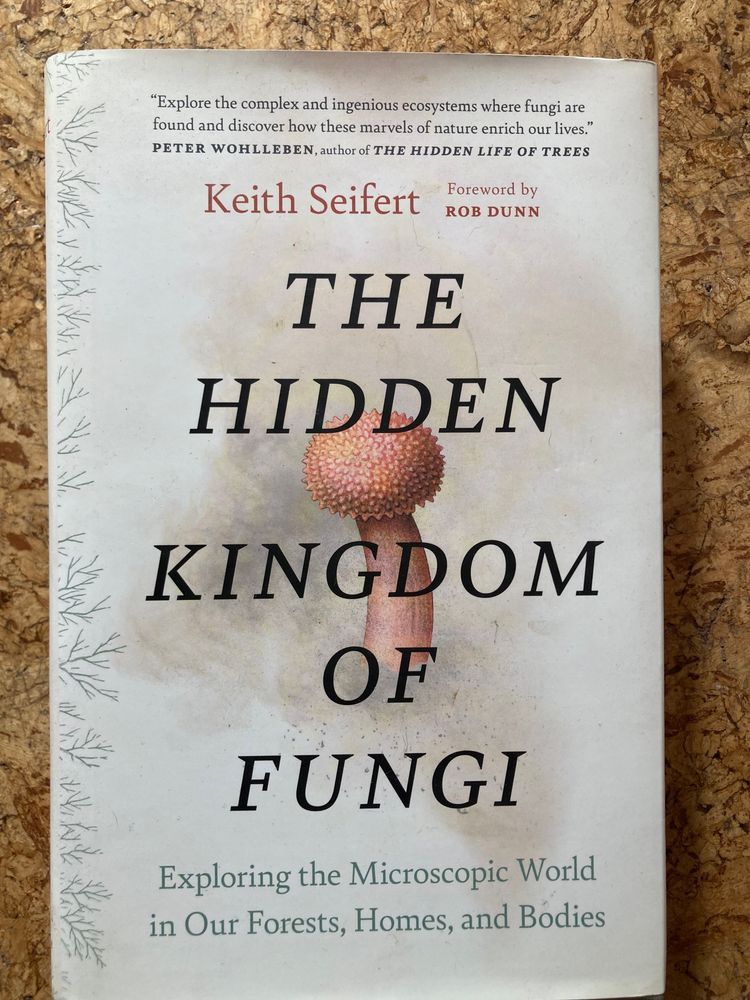 Book cover of The Hidden Kingdom of Fungi by Keith Seifert, featuring a pale cream background with subtle branch-like patterns and an illustration of a reddish spore structure. The subtitle reads: Exploring the Microscopic World in Our Forests, Homes, and Bodies.