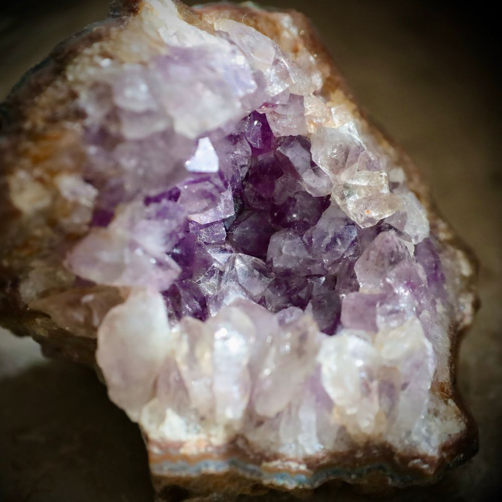 Eine kleine Amethystdruse mit violetten Kristallen im Inneren, weißen am äußeren Rand und einer grün-braunen Außenschicht.