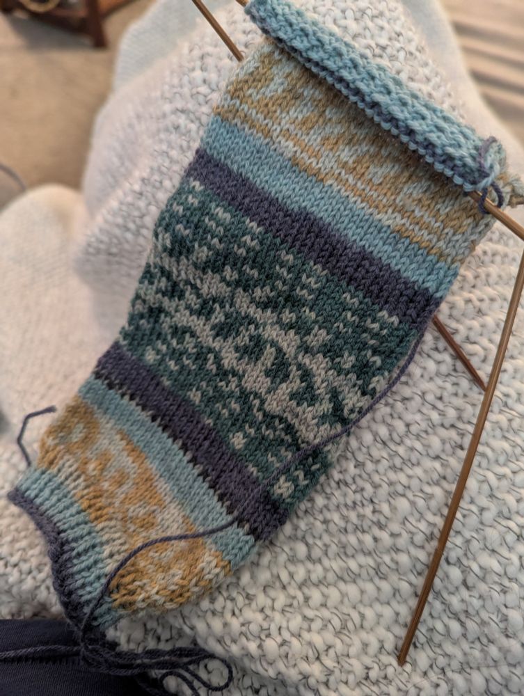 Sock knitting project in progress with bamboo needles. The yarn is a blue green and gold pattern.