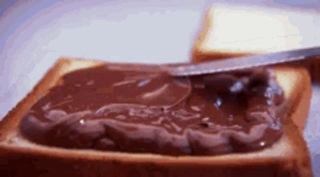 a knife is spreading chocolate spread on a piece of bread