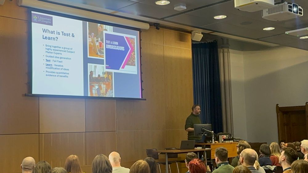 Man presenting to a large audience in front of a screen. 