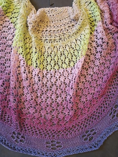 Semi circular shawl in a gradient from light green to pink to violet to blue/purple. Main body in a diamond shape lace; edging with eyelets in a daisy shape 