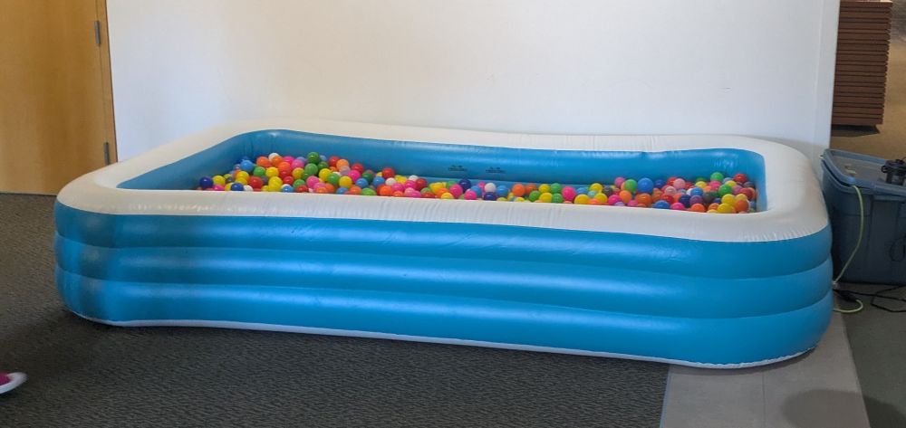 a makeshift ball pit: blue and white medium sized inflatable pool filled with plastic balls of assorted colors