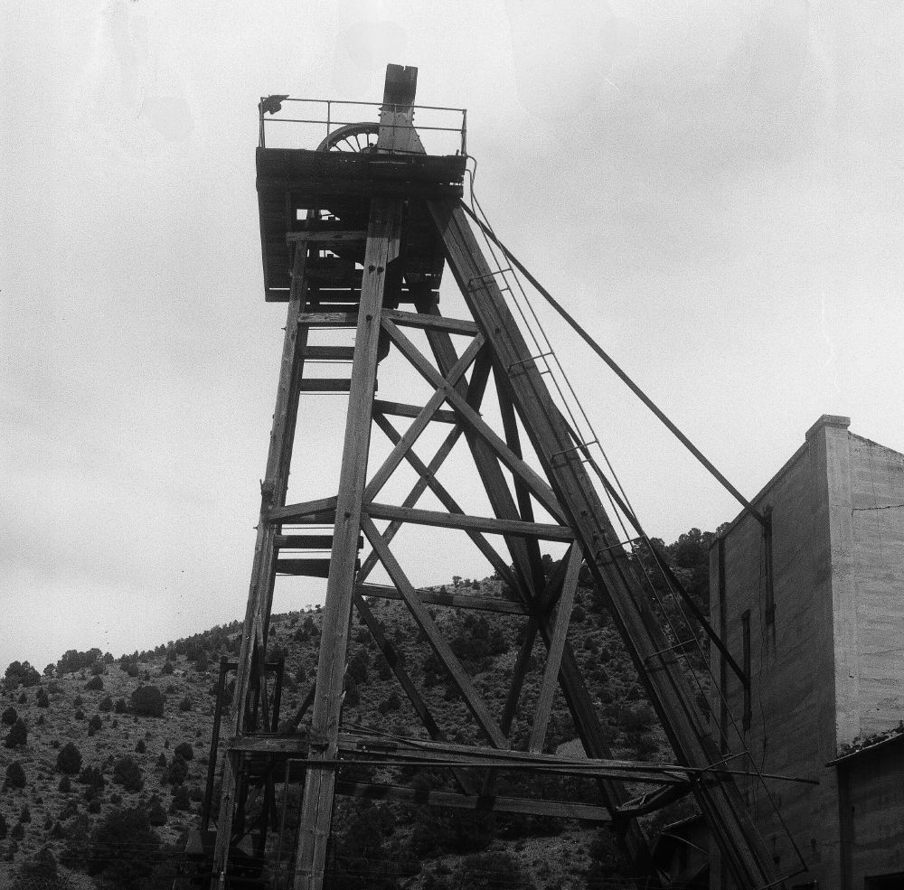 timber mining headframe with a mountainside in the background and a light shaded brick winder building to the right