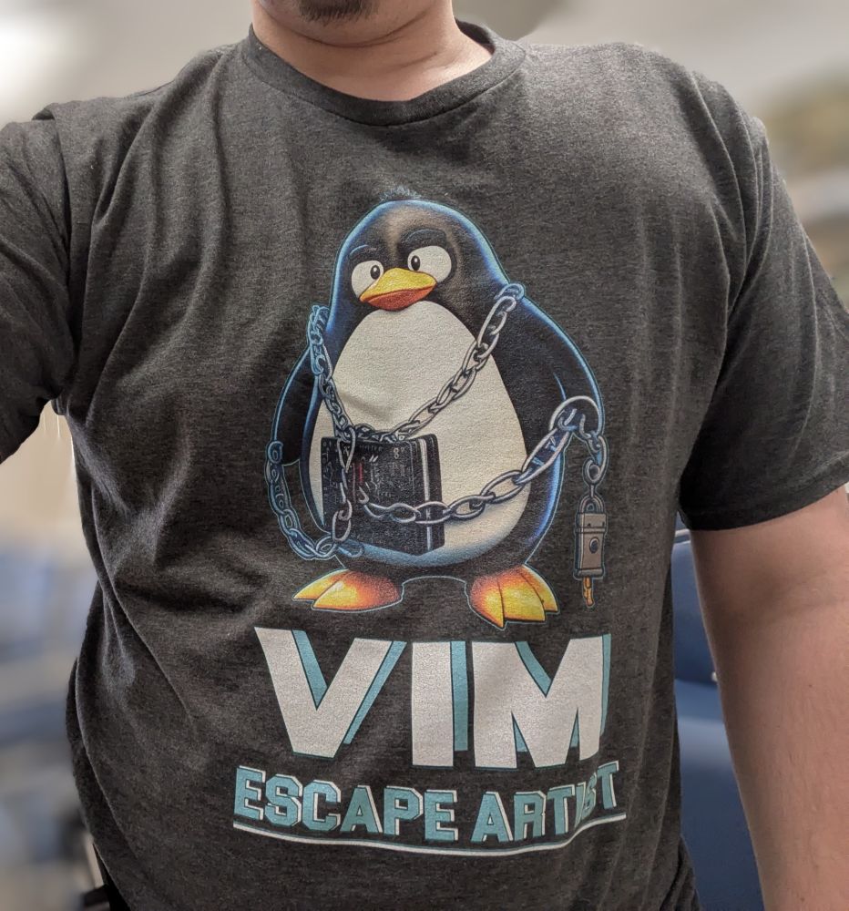 Grey shirt with penguin wearing lock and chain. Text below reads, "Vim Escape Artist".