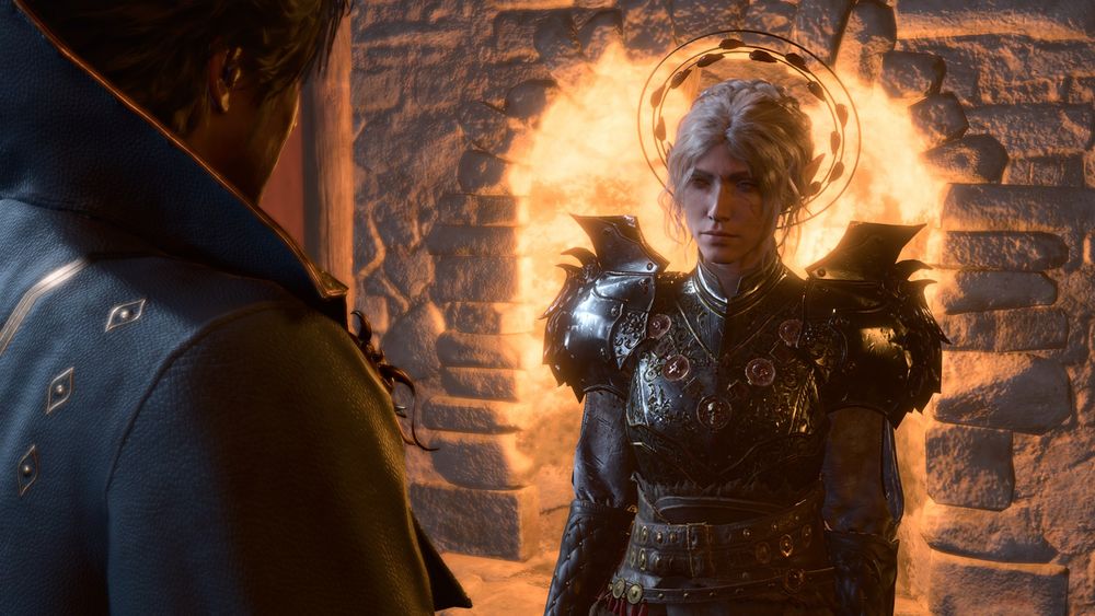 An in-game screenshot of my durge Amarie and Gortash. Amarie is an elf with a pallid skintone and bone white hair done up in a messy crown braid; attached to the back of her hair is a large hairpiece resembling the symbol of Bhaal. She is wearing dark armor with large spiked pauldrons along with cloth sleeves, leather bracers, and a leather belt. She is standing slightly to to the right of the center of the frame and is standing in front of a fireplace. Gortash is wearing his default outfit and takes up most of the left side of the frame. Gortash is facing away from the viewer and his face is obscured while Amarie is facing the viewer and her face is fully in the frame. Amarie is looking at Gortash with a kind of serious yet tender expression on her face.